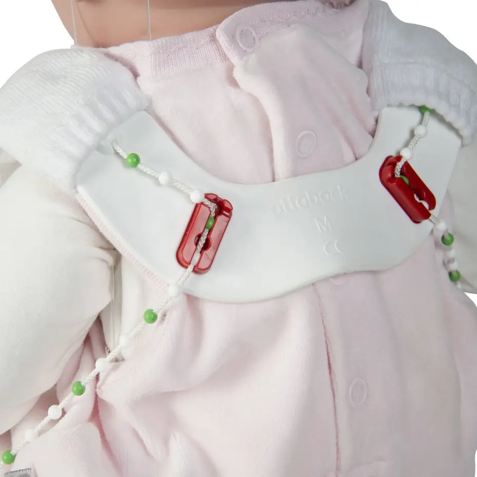 Widok z bliska lalki niemowlaka z założoną szyną bioderkową typu Tübinger: zakresy ustawień i zamykania na plecach